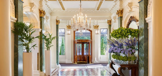 luxury hotel foyer, with diamond patterned marble floor, large glass chandelier, and on the right and left of the corridor has vases of flowers